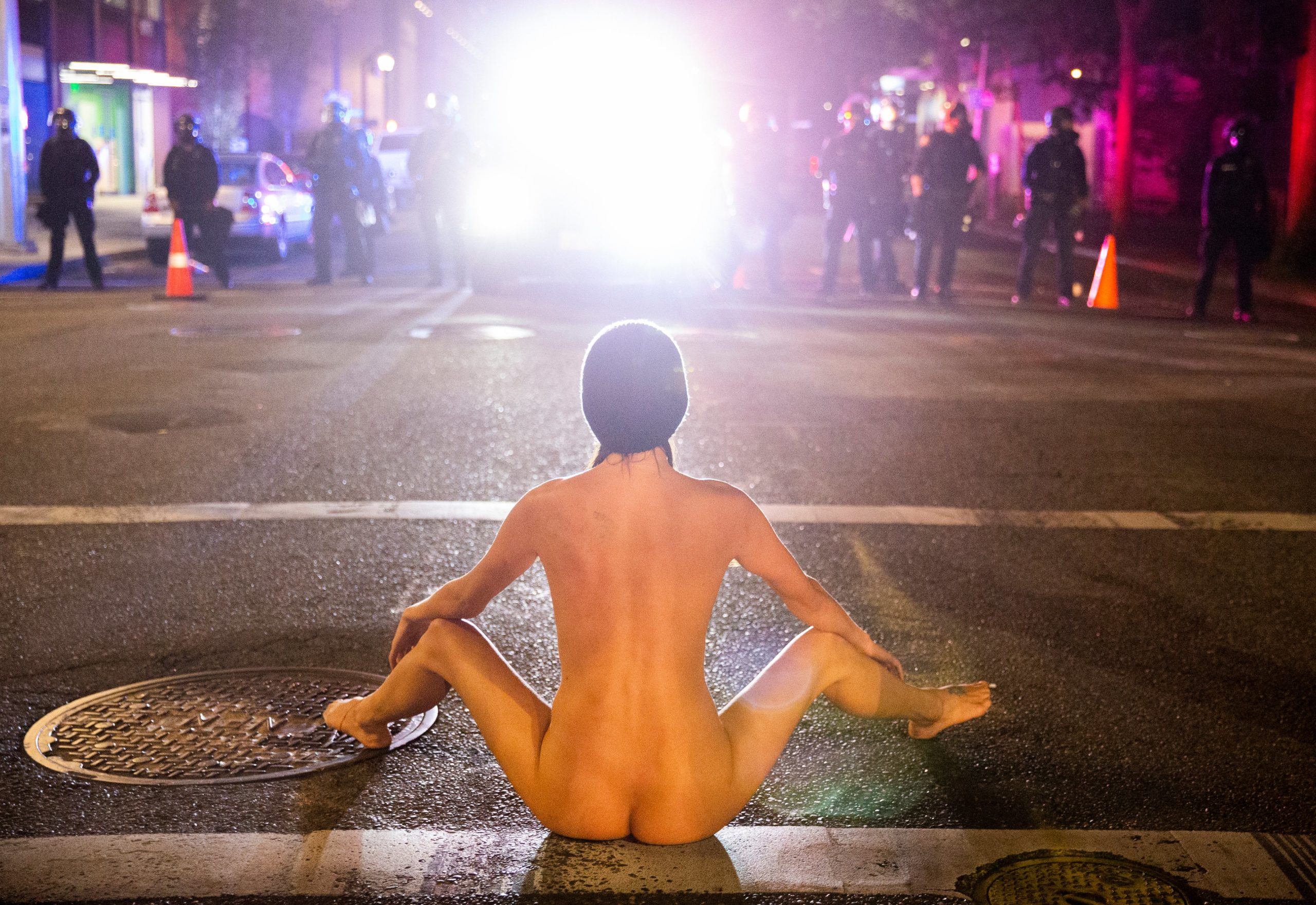 A naked protester sits in front of police